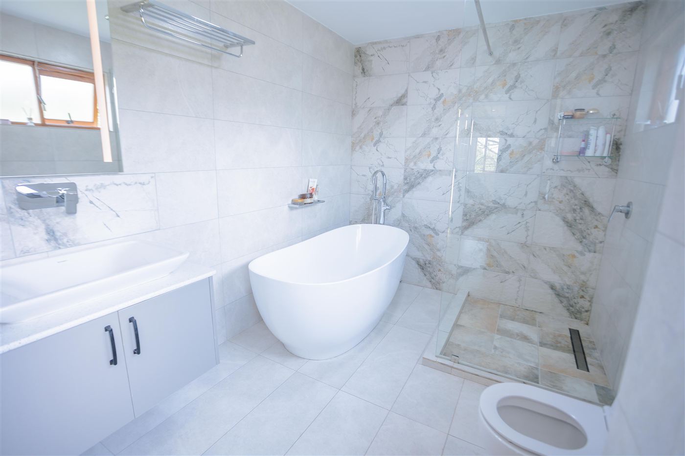 Freestanding bathtub against marble-tiled wall beside a glass shower