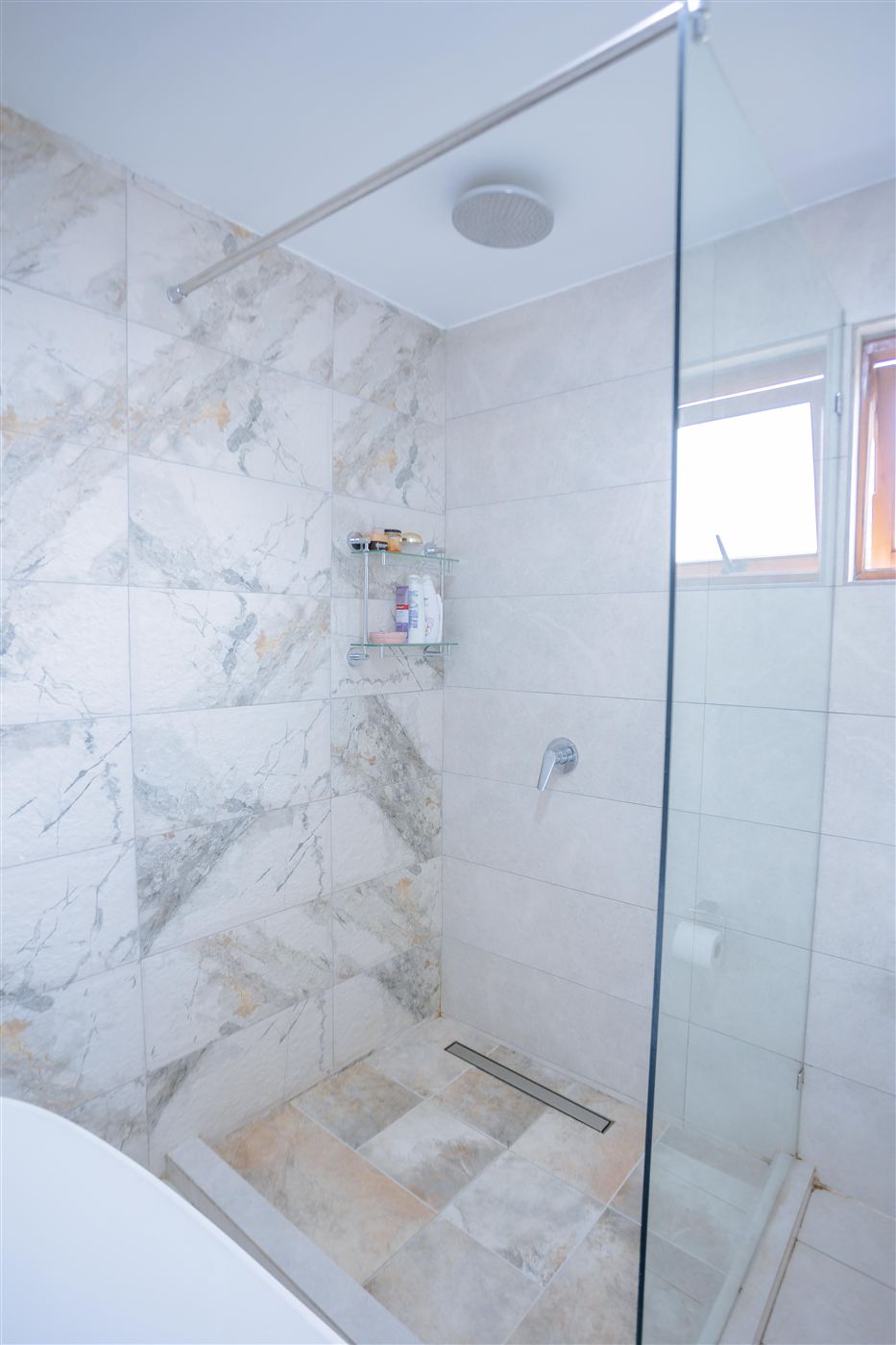 Walk-in glass shower with rainfall shower head and marble tiling
