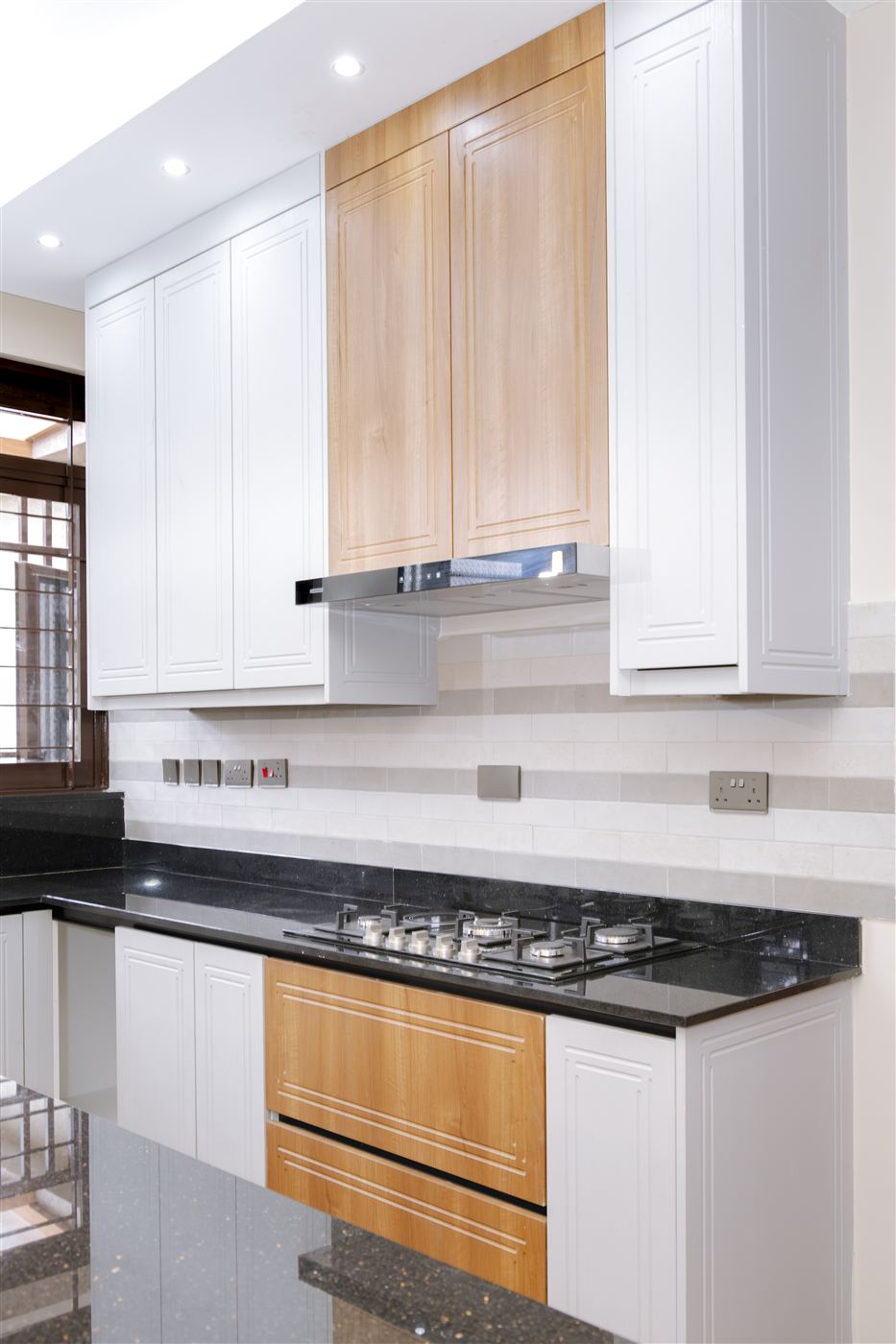 Close-up of gas hob and range hood with wood and white cabinetry